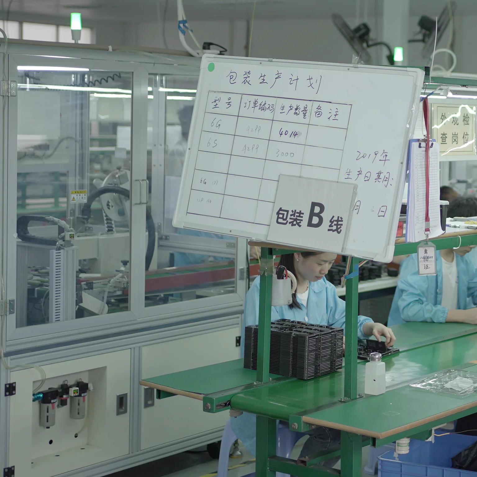 Assembly line at the Hitama plant: operators at their stations, with the handwritten production-plan board for line B in the foreground